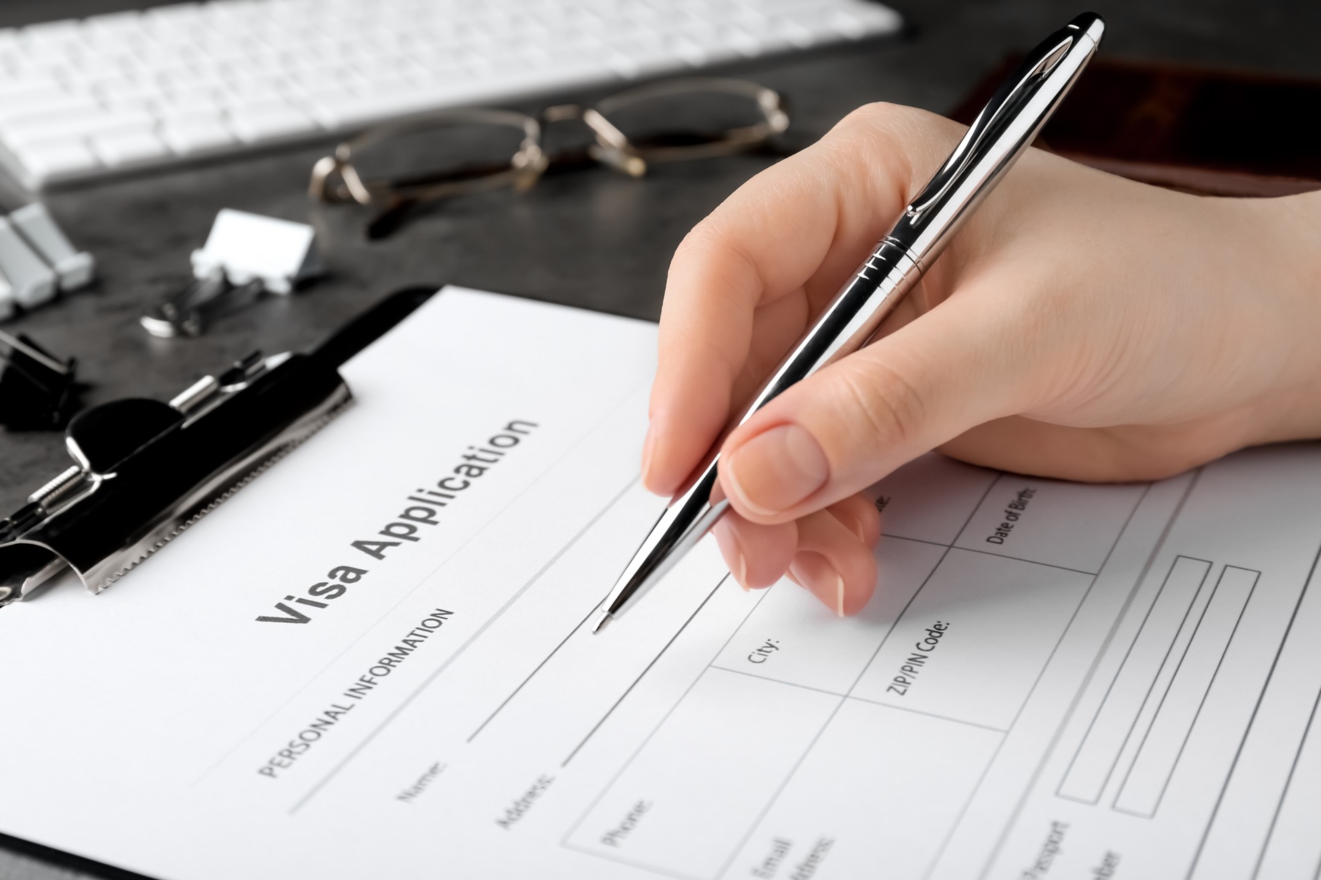 Woman filling visa application form for immigration at grey table, closeup